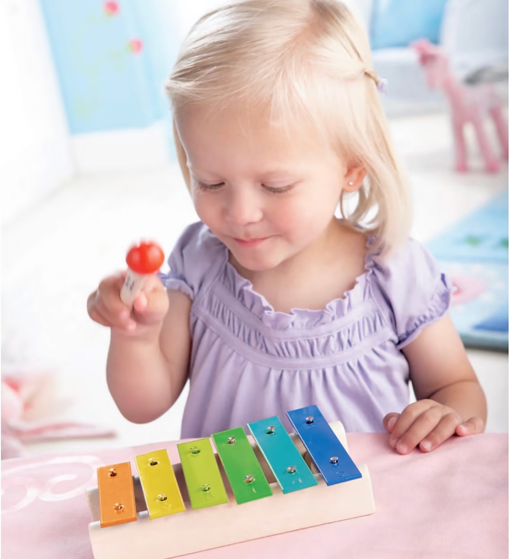  Xylophone Toy Instrument. A wooden drumming stick on top of a row of colourful flat metal bars pinned into a wooden base with each one being a different musical note