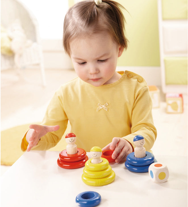 A child playing with the yellow, red and blue Haba wooden ring toss game and  a wooden dice 