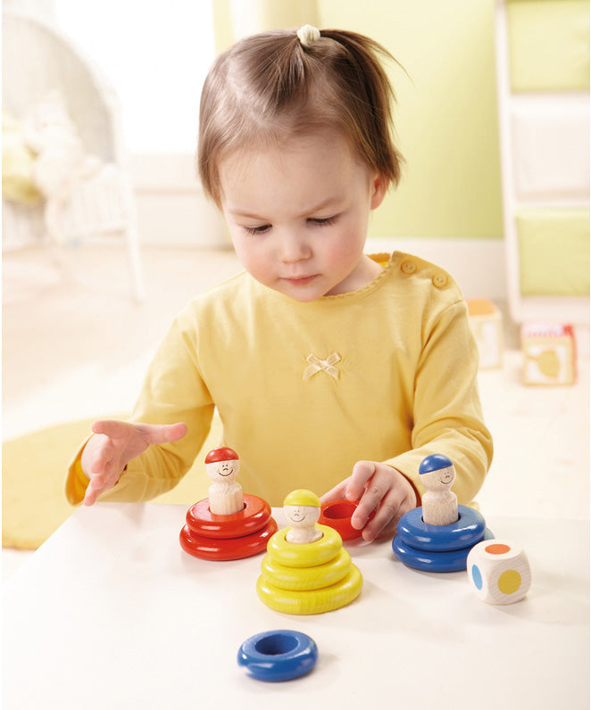 A child playing with the yellow, red and blue Haba wooden ring toss game and  a wooden dice 