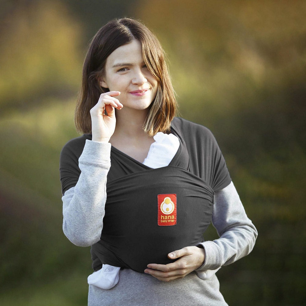 Woman wearing the Hana organic charcoal baby carrier in front of a green background