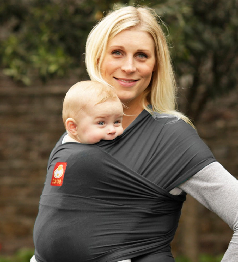 Woman carrying baby in the charcoal Hana baby carrier in front of a grey background