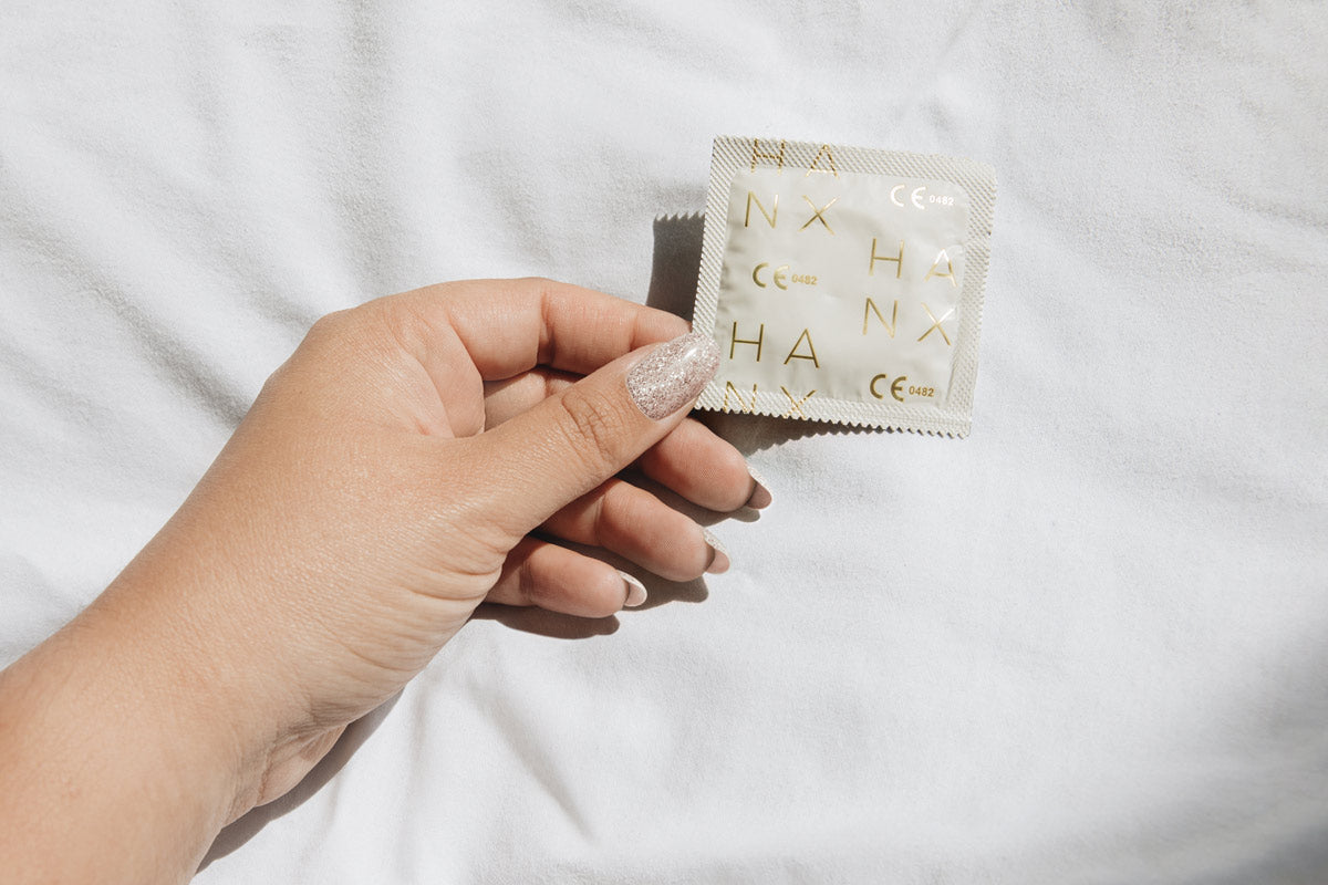 Close up of a hand holding a Hanx Vegan latex condom on a white sheet