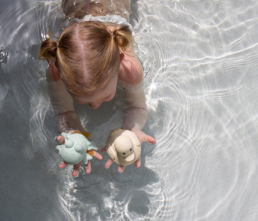 Hevea Upcycled rubber sand duck and sage frog toys being played in the pool by a small child