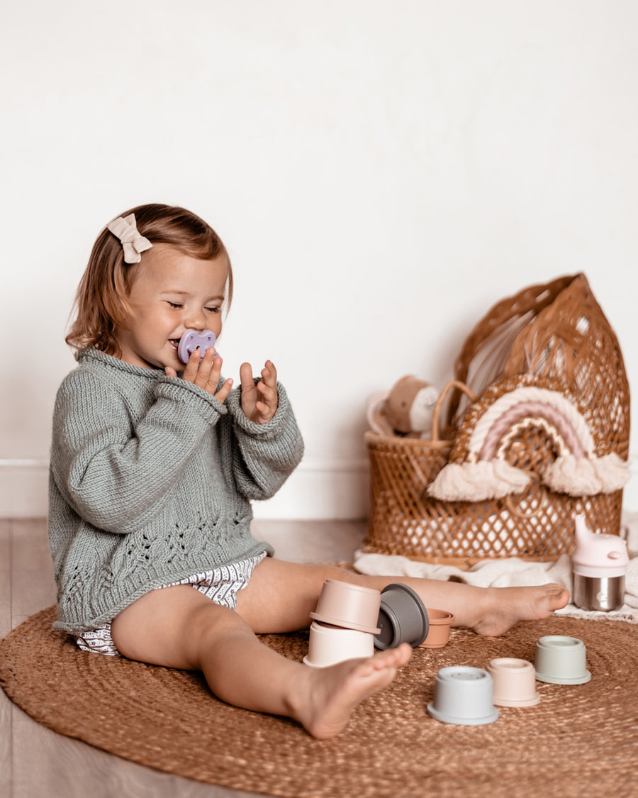 Girl sat on the floor laughing with a Hevea natural rubber pacifier in her mouth