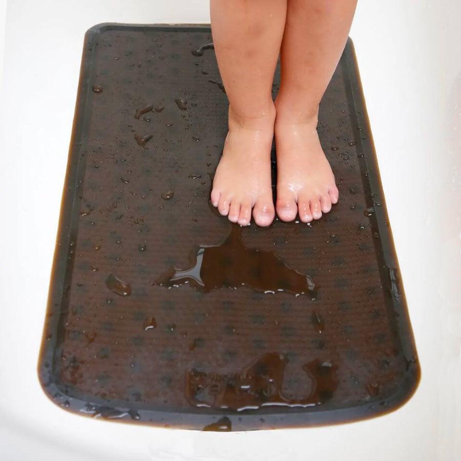 Close up of a child's feet stood on the Hevea plastic-free rubber bath mat on a white background