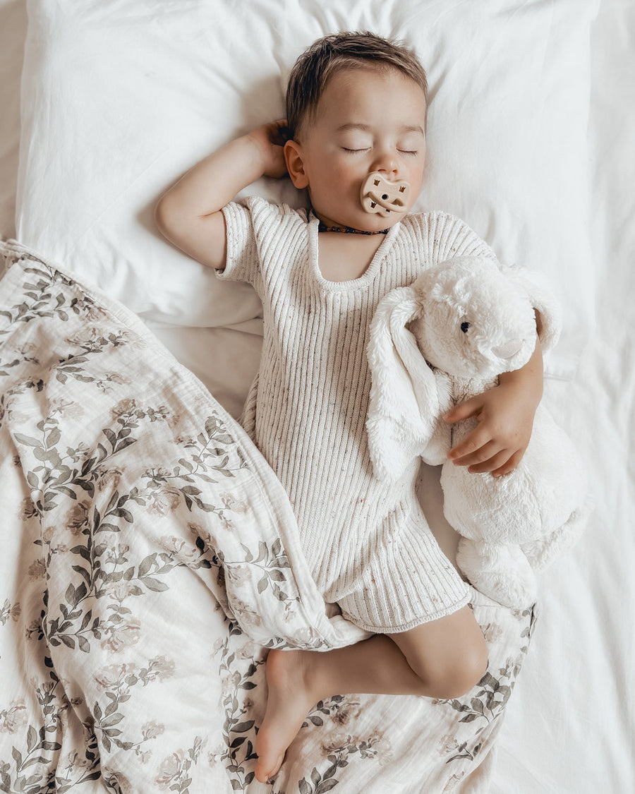 Young boy laying on a white bed with a Hevea natural rubber dummy in his mouth