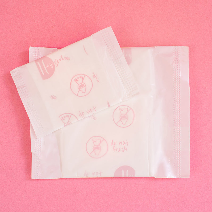 Hey Girls Natural Bamboo & Corn Fibre Disposable Overnight Pad open in someones hand on a pink and red background