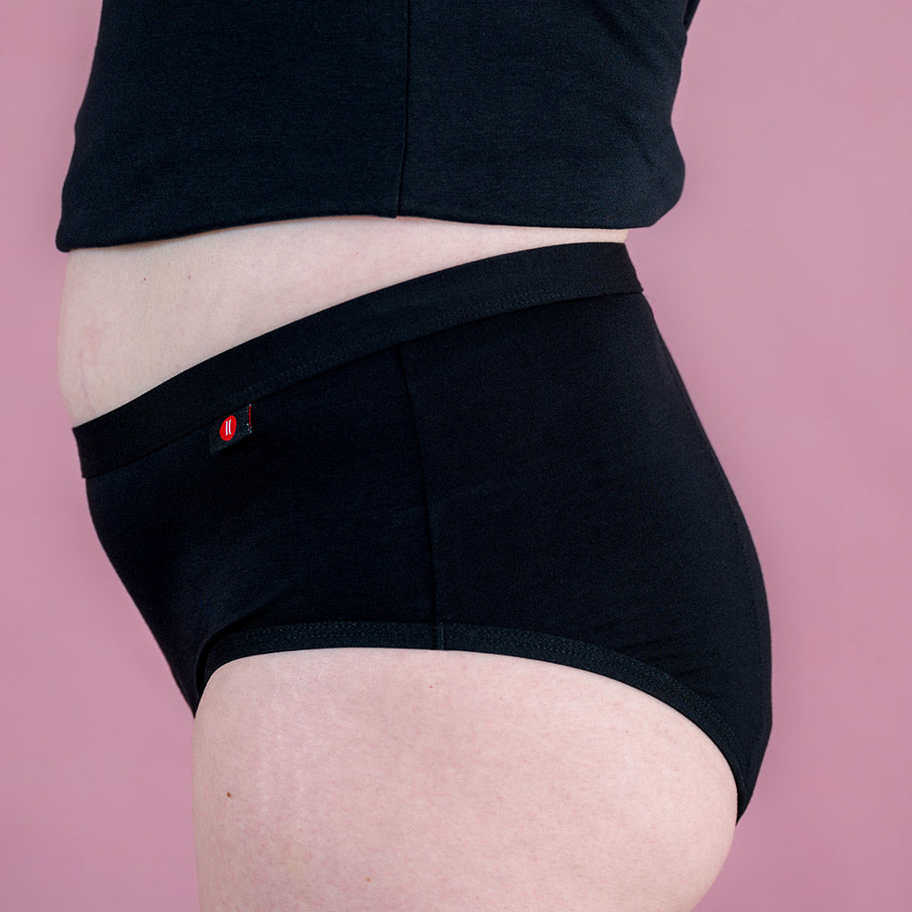 Hey Girls Mid Waist Black Reusable Period Pants worn by a person with a black top against a pink background