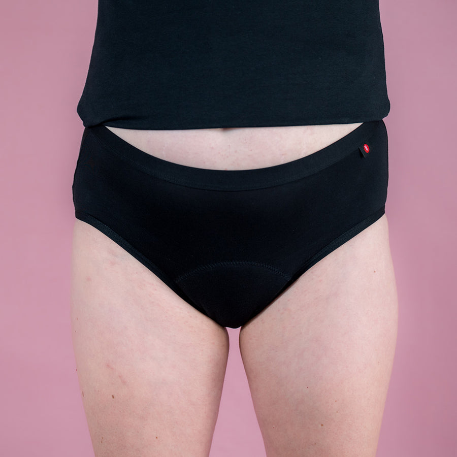 Hey Girls Mid Waist Black Reusable Period Pants worn by a person with a black top against a pink background