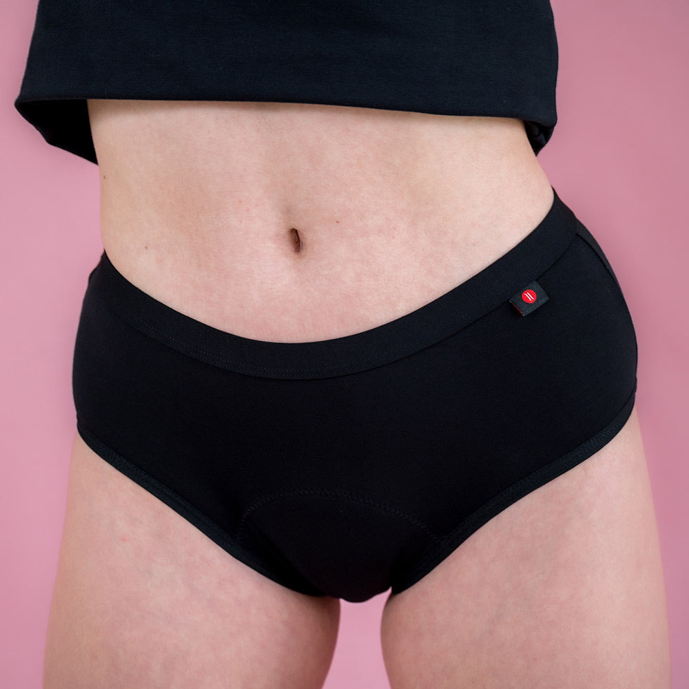 Hey Girls Mid Waist Black Reusable Period Pants worn by a person with a black top against a pink background