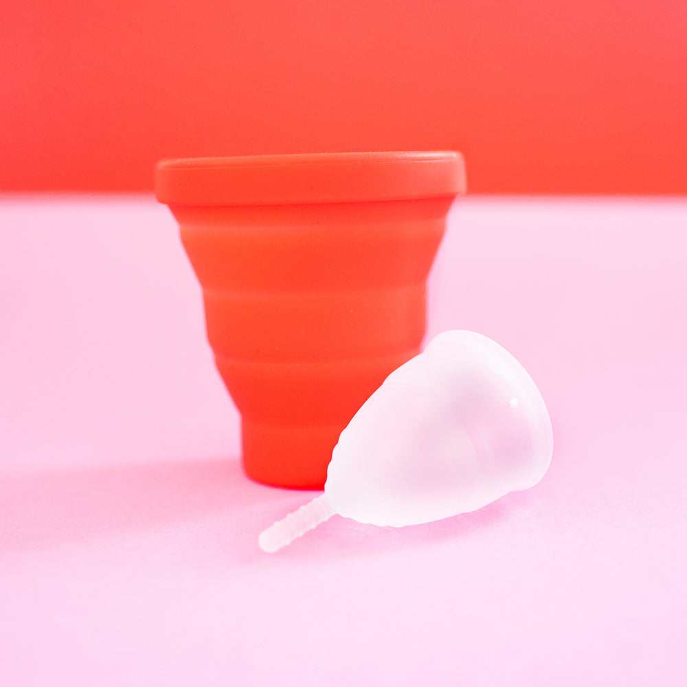 Hey Girls red Menstrual Cup Sterilising Pot with a small white menstrual cup on a pink and red background