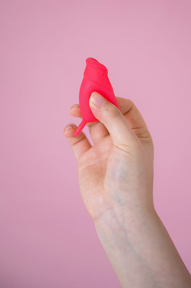 Hey Girls Large red Silicone Menstrual Cup folded in someone's hand on a pink background