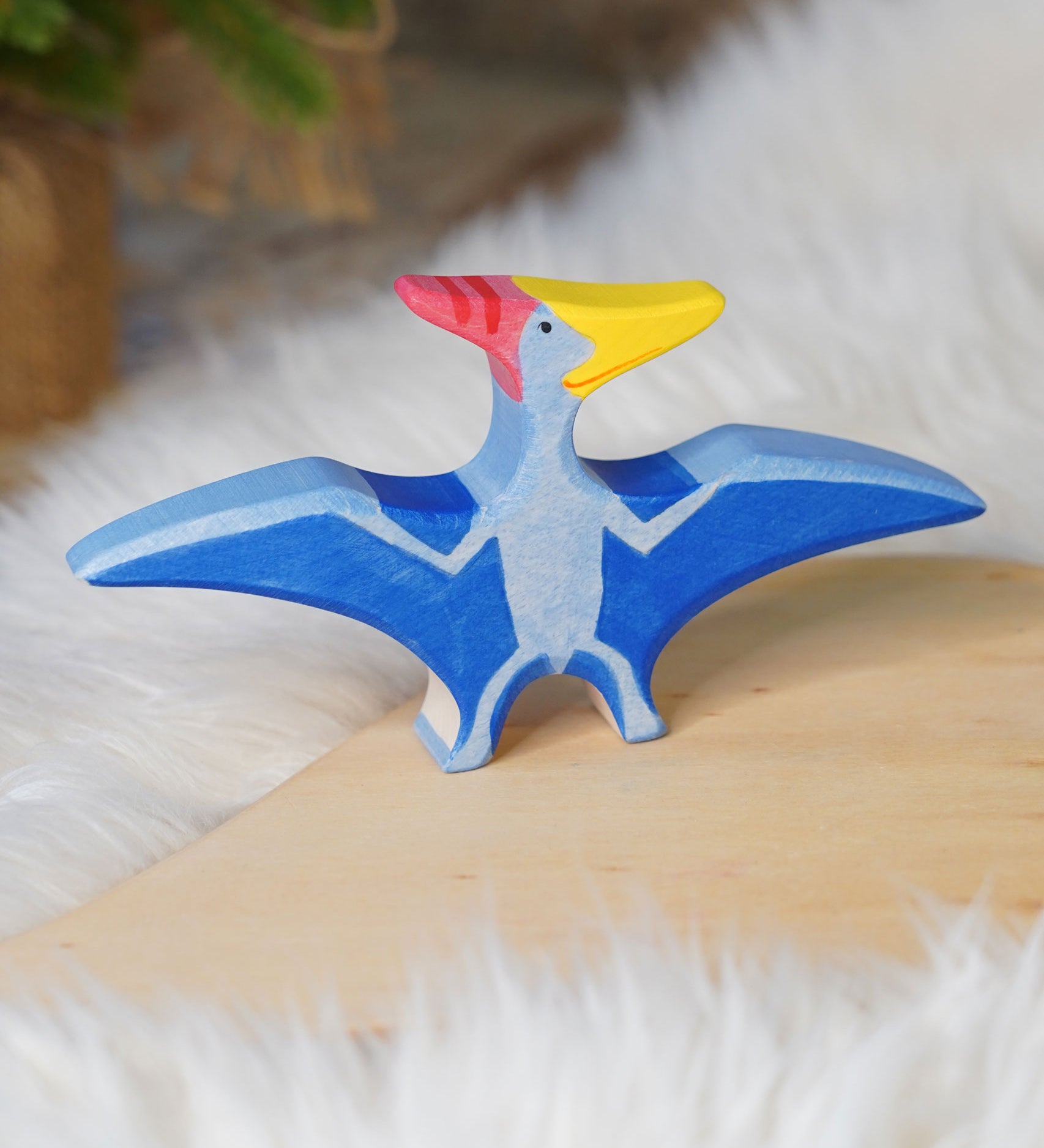 Holztiger Pteranodon pictured on a wooden play platform with white fluffy fabric behind. A blue flying dinosaur figure with handpainted details.