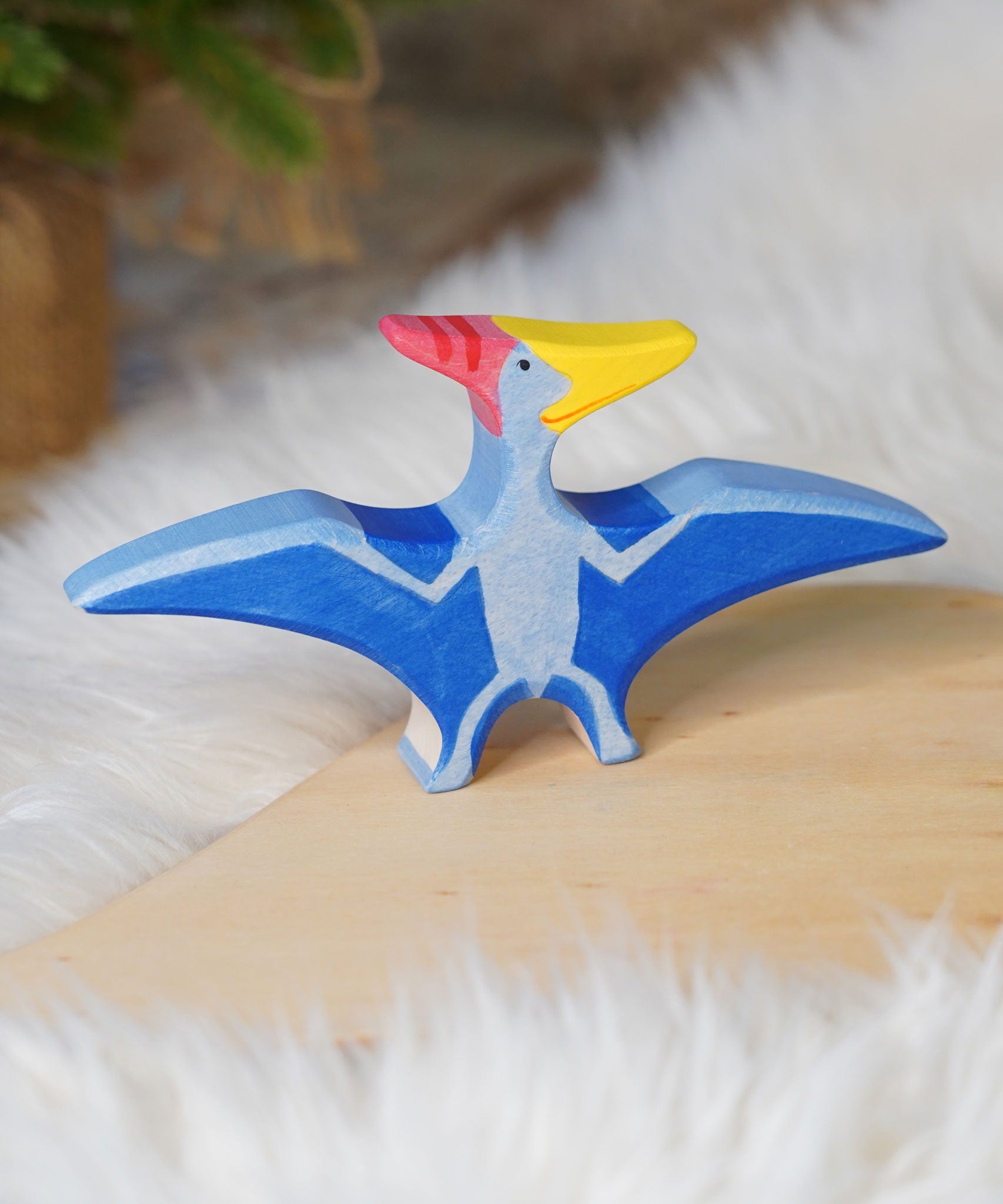 Holztiger Pteranodon pictured on a wooden play platform with white fluffy fabric behind. A blue flying dinosaur figure with handpainted details.