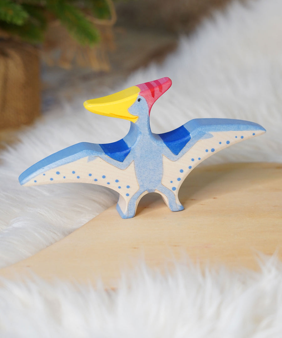 Holztiger Pteranodon pictured on a wooden play platform with white fluffy fabric behind. A blue flying dinosaur figure with handpainted details.