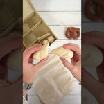 Looking down at child using the Plan Toys wooden knife to cut the wooden bread toy set on a wooden worktop