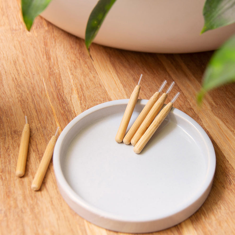 Hydrophil Bamboo Interdental sticks on a white ceramic tray on a wooden worktop.