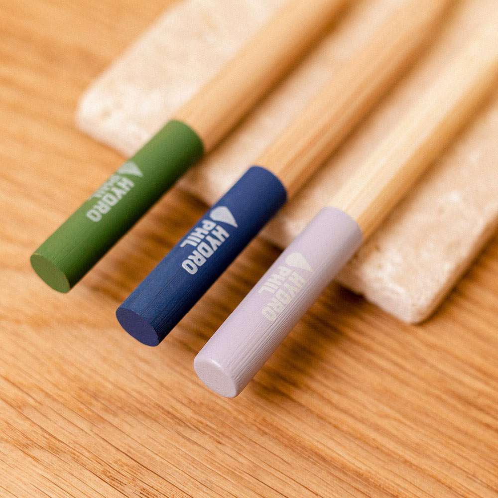 Coloured Hydrophil Bamboo toothrbrushes lined up on a stone tray on a wooden worktop.