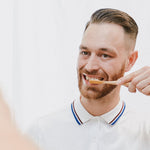 Man brushing teeth with the Hydrophil bamboo eco toothbrush in the mirror.