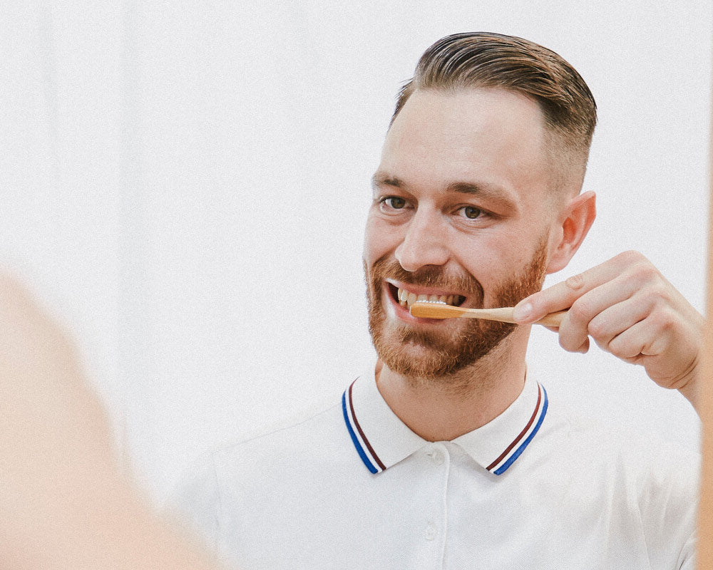 Man brushing teeth with the Hydrophil bamboo eco toothbrush in the mirror.