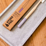 Purple Hydrophil Bamboo toothbrush on a stone tray on a wooden worktop.