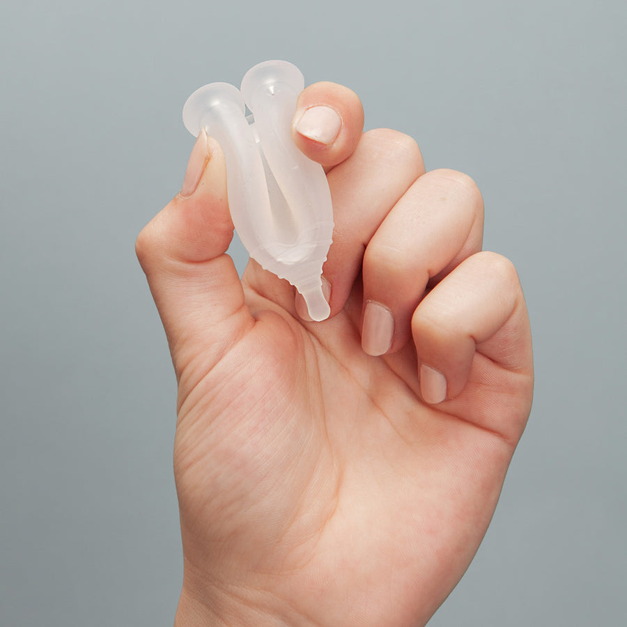 Close up of a hand folding an imse vimse eco-friendly reusable menstrual cup on a grey background