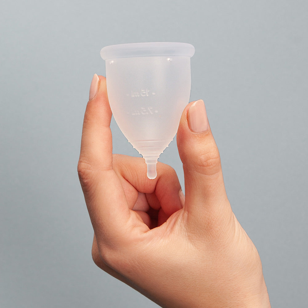 Close up of a hand holding an imse vimse eco-friendly period cup on a grey background