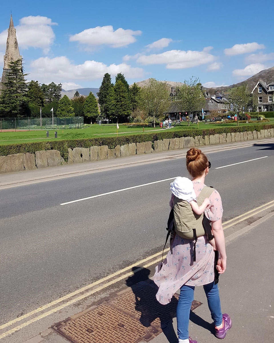 person babywearing on the back using an Integra baby carrier in a sage green colour way