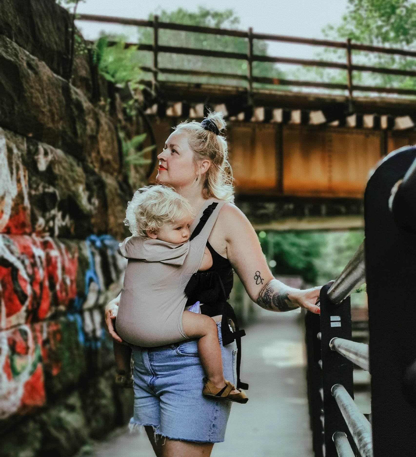 A person wearing the Integra Size 3 Taupe Regular Strap Baby Carrier whilst walking outside