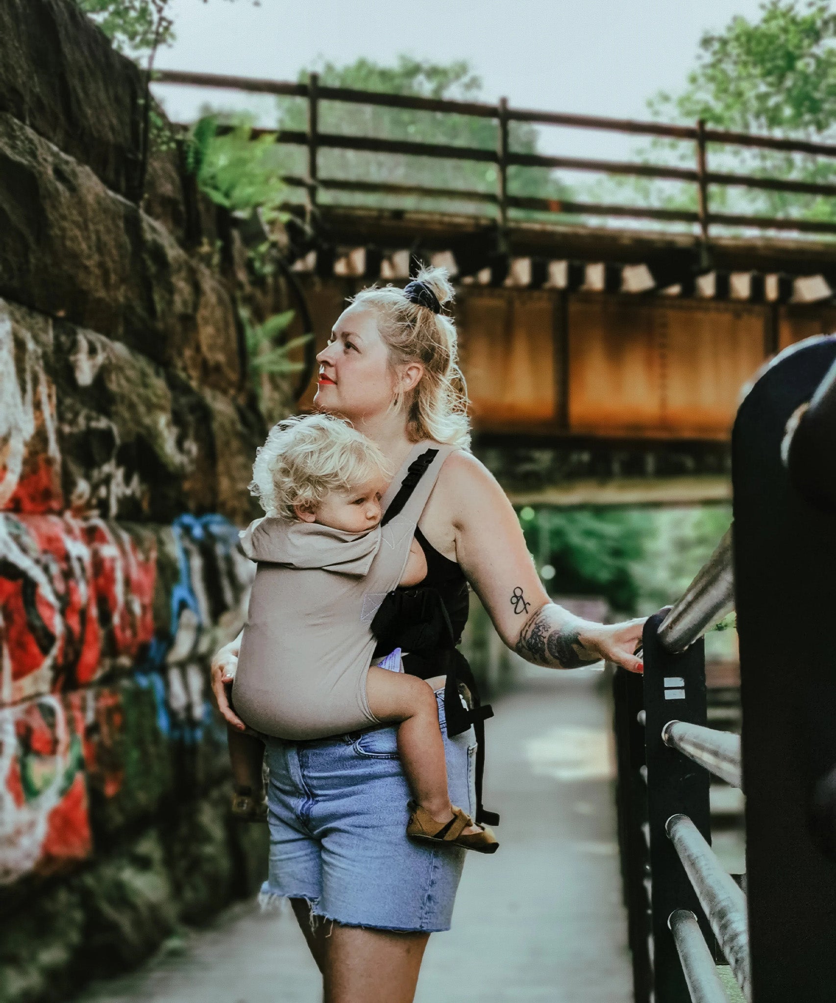 A person wearing the Integra Size 3 Taupe Regular Strap Baby Carrier whilst walking outside