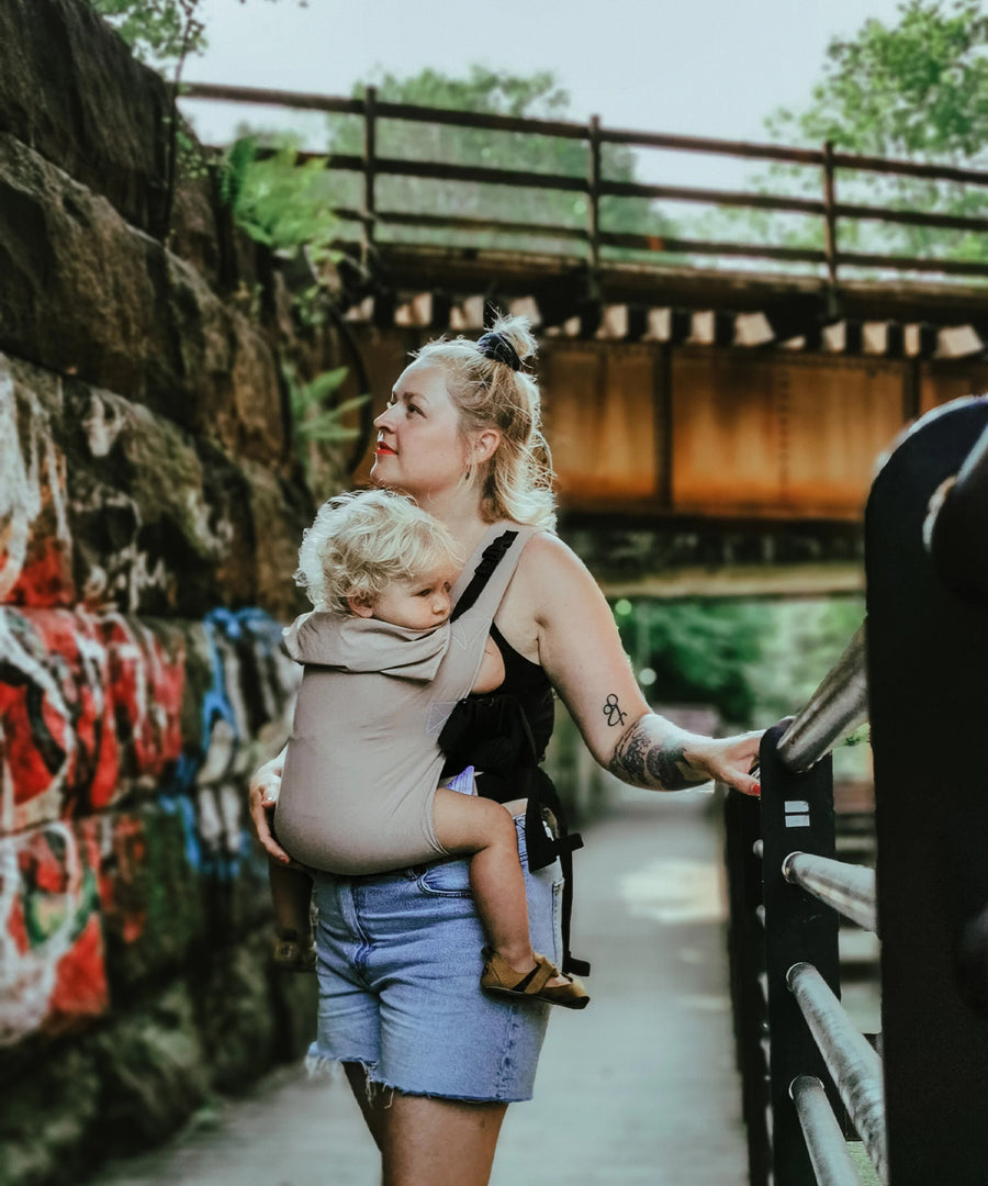 A person wearing the Integra Size 3 Taupe Regular Strap Baby Carrier with a child inside