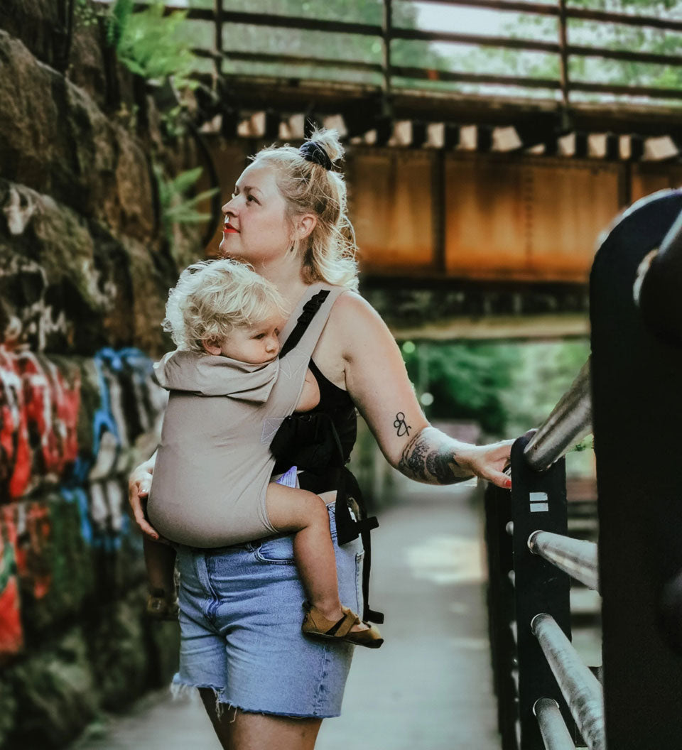 person babywearing on their front using a taupe coloured Integra baby carrier