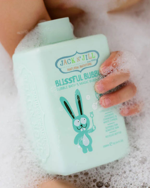 Child holding botttle of Jack N' Jill Blissful Bubbles Bubble Bath with Bubble Wand in their hand covered in bubbles