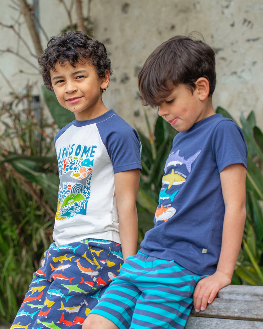 A child happily wearing the Frugi Avery Applique T-Shirt - Sharks. A deep Navy Blue short sleeve t-shirt made from GOTS organic cotton