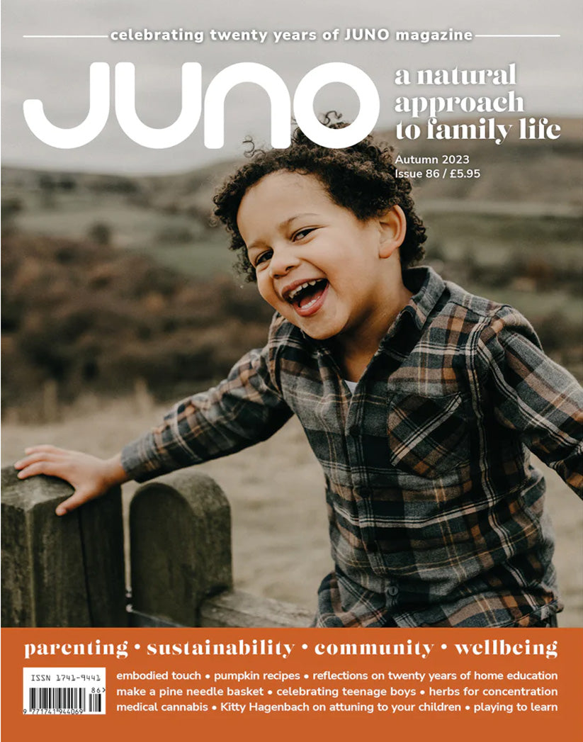 Juno Magazine cover pictures a young child on a beach with their toes in the sand and the water lapping at their feet.