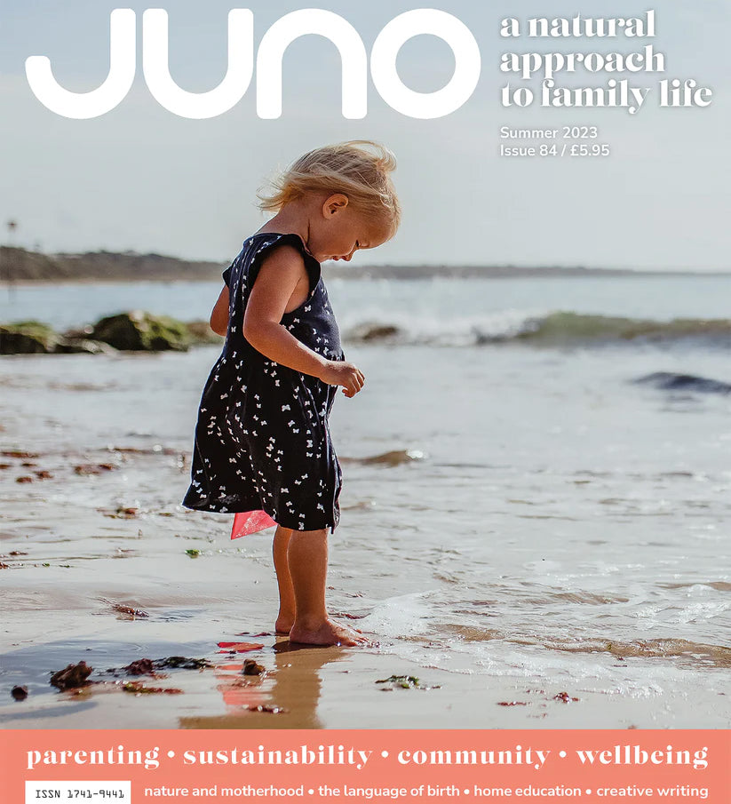 Juno Magazine cover pictures a young child on a beach with their toes in the sand and the water lapping at their feet.