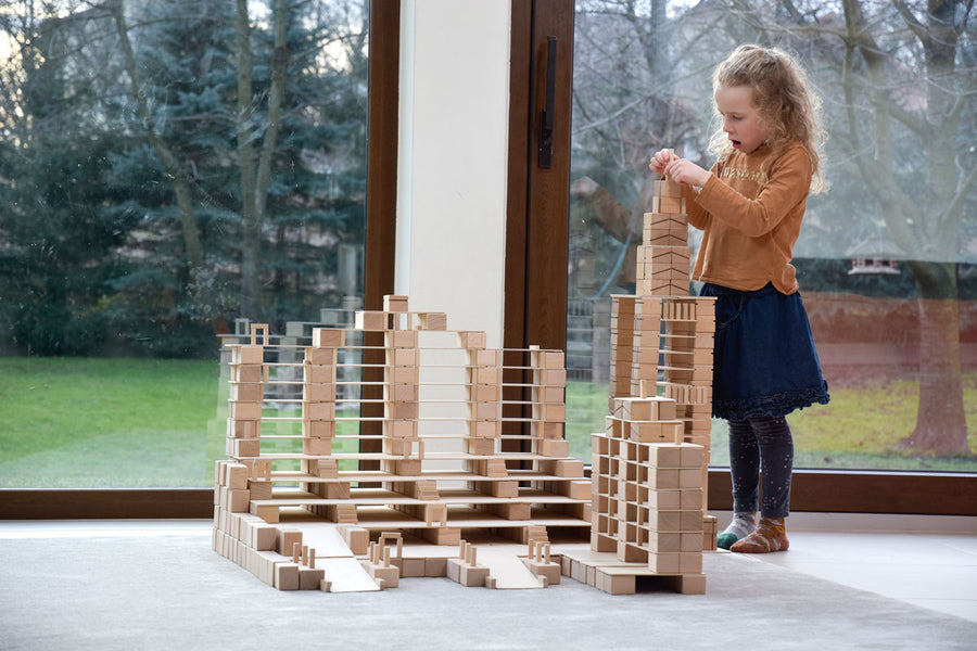 Girl stacking up Just Blocks plastic-free wooden shapes in a large tower on a grey carpet