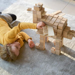 Girl laying on a grey carpet playing with some Just Blocks