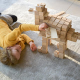 Girl laying on a grey carpet playing with some Just Blocks