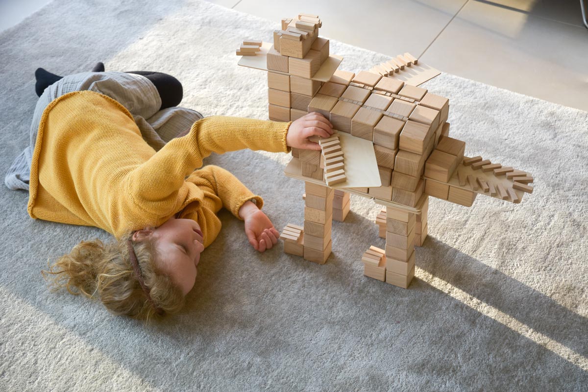 Girl laying on a grey carpet playing with some Just Blocks