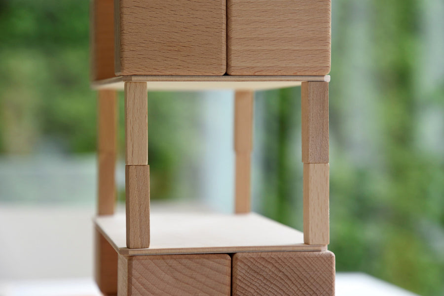 Just Blocks wooden waldorf toy shapes stacked in the shape of an Eiffel Tower on a grey carpet