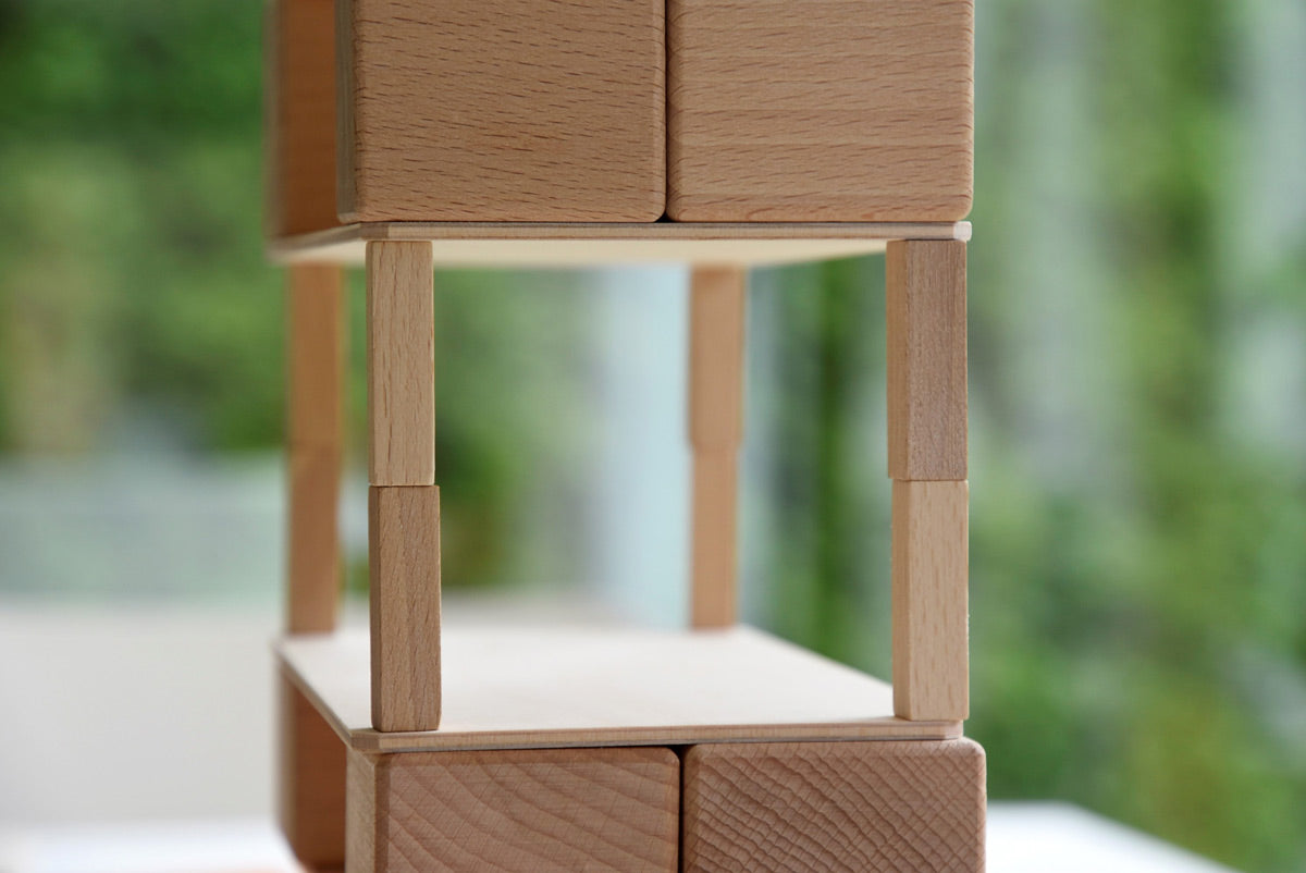 Just Blocks wooden waldorf toy shapes stacked in the shape of an Eiffel Tower on a grey carpet