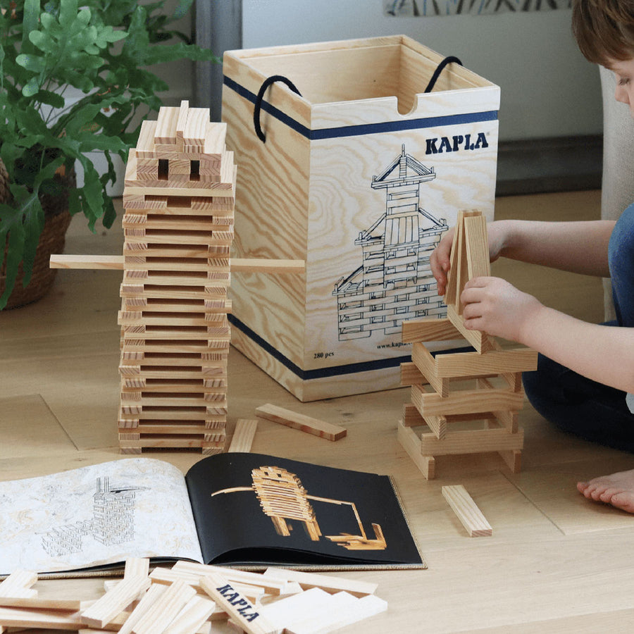 Child crouched down building a tower with Kapla Waldorf building blocks