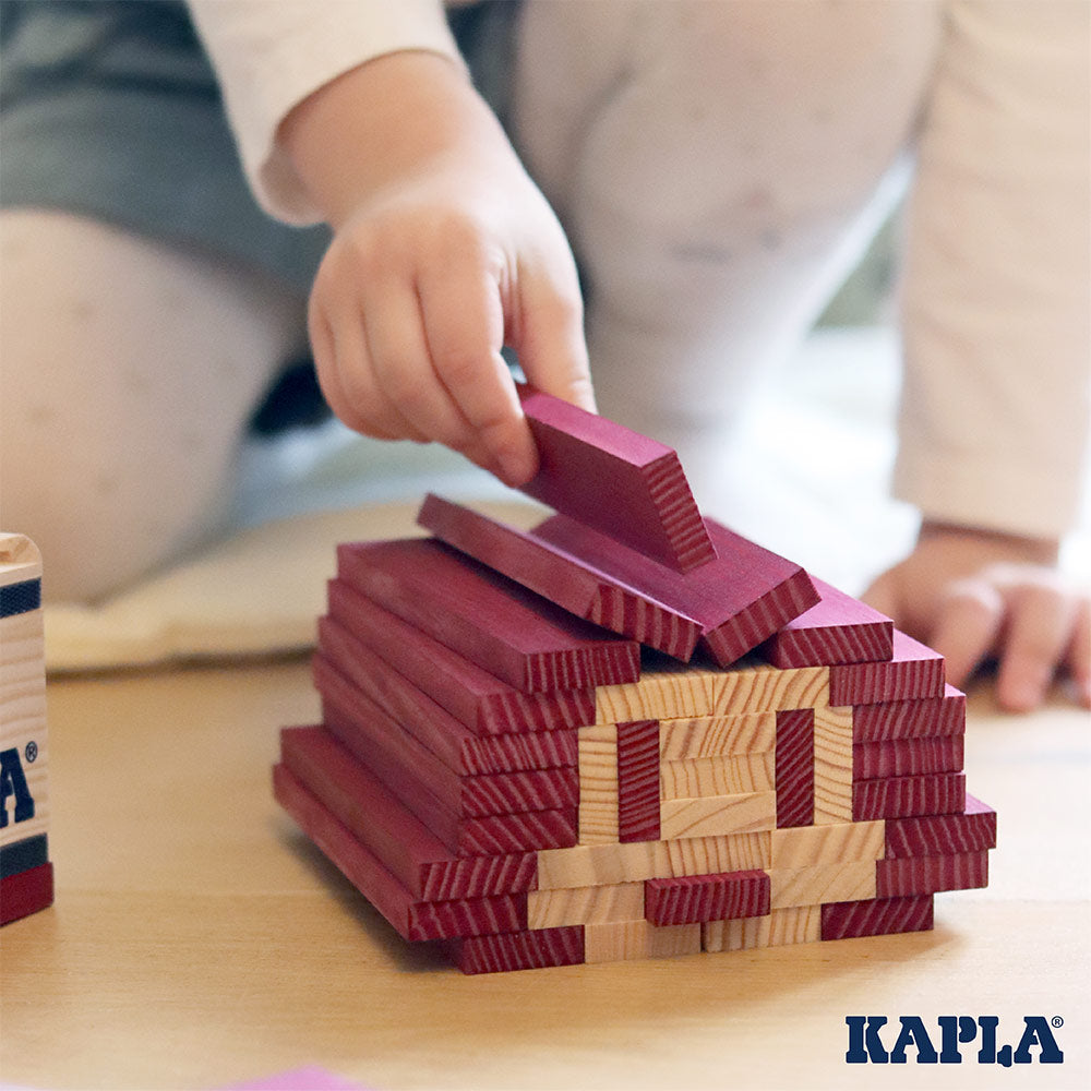 Close up of child's hand placing a Kapla eco-friendly wooden block on top of a wooden stack