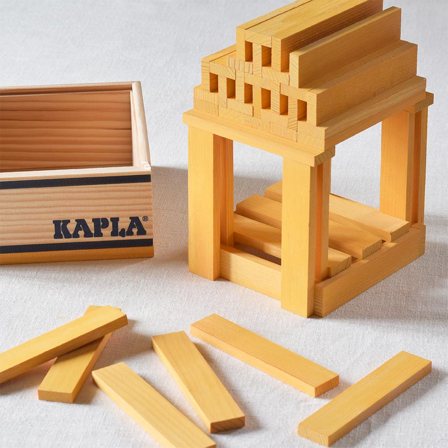 Close up of the yellow Kapla building blocks stacked into a small temple shape on a grey fabric background