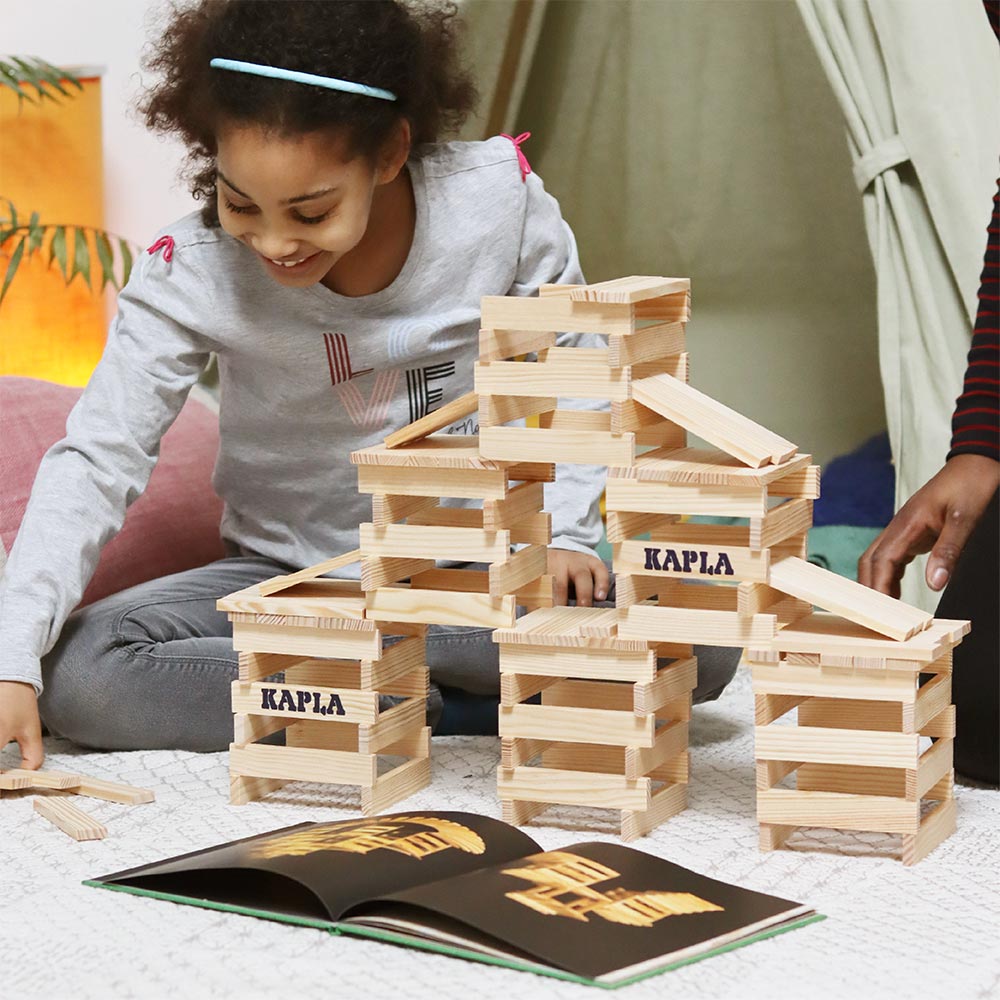 Girl building a wooden stack of Kapla building blocks using the Kapla simple architecture book