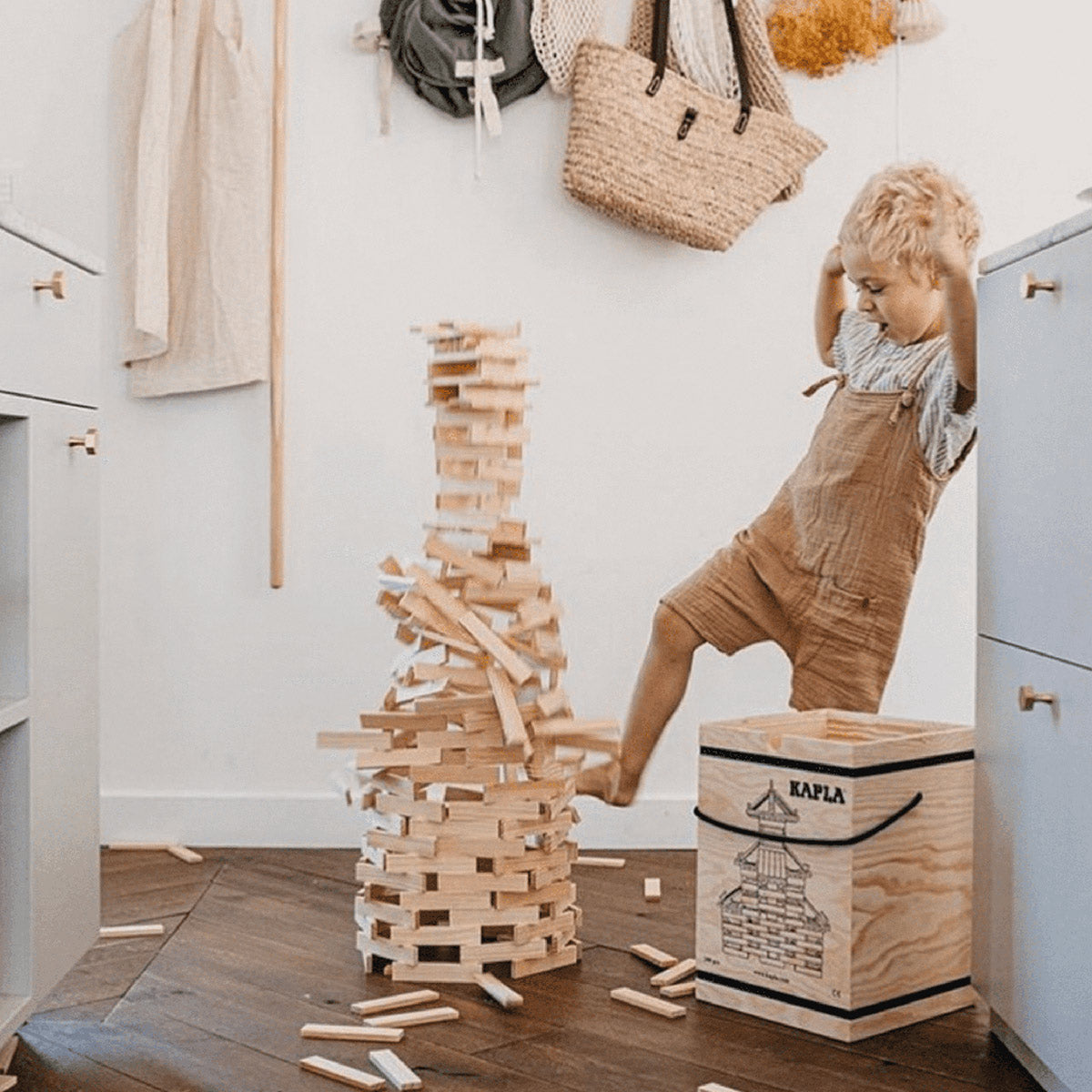 Boy stood next to a falling tower of Kapla plastic-free toy blocks