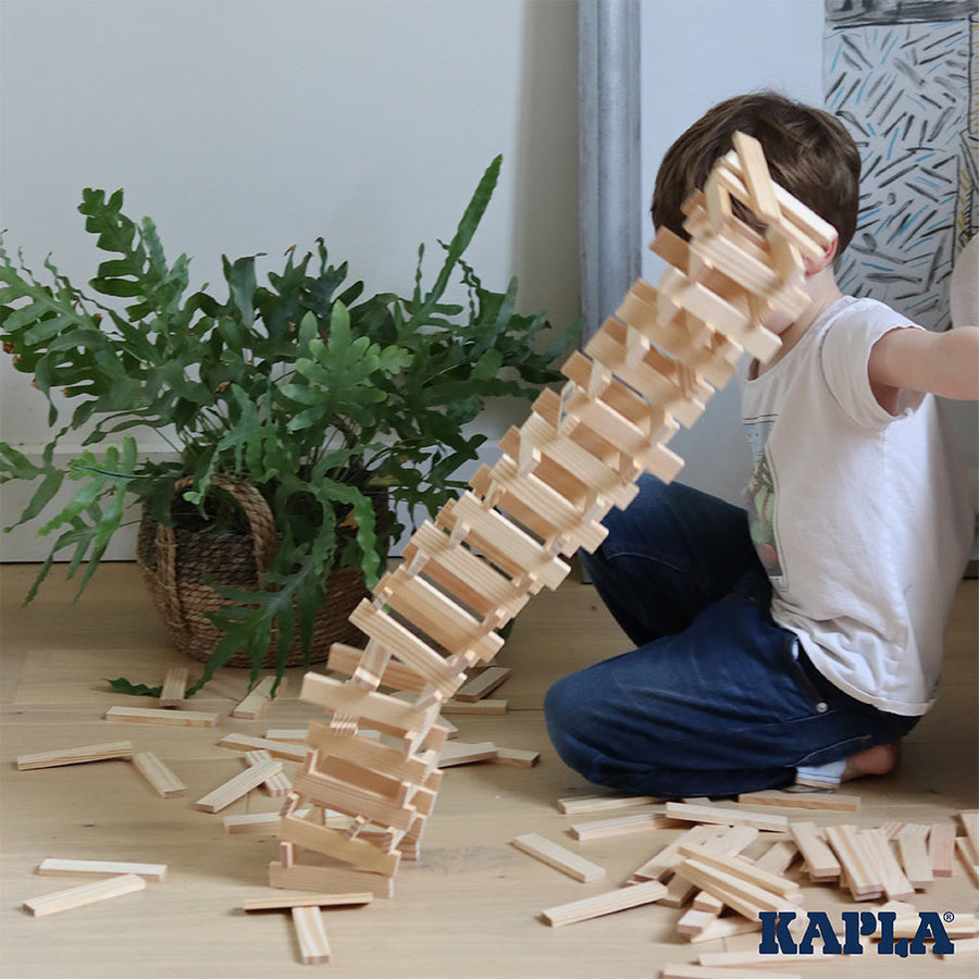 Giant tower of Kapla natural wooden stacking blocks falling over on a wooden floor