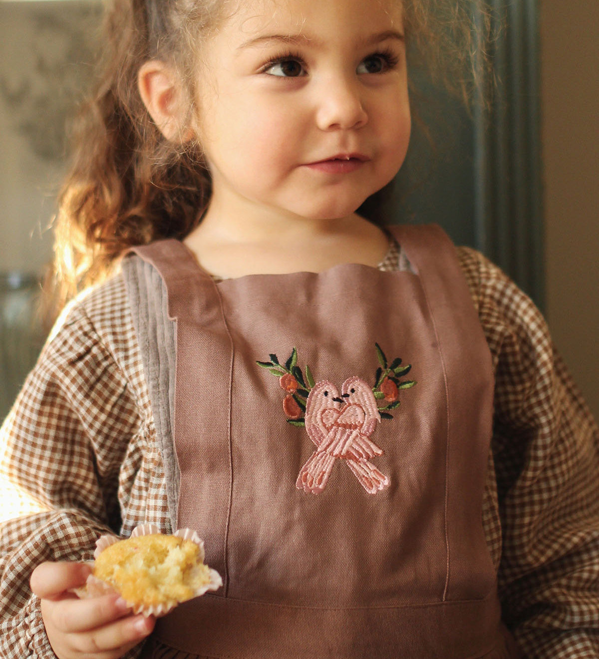 dusky pink pinafore apron with two delicately embroidered pink love birds on the chest panel. Loosely pleated with two pockets on either side of the pinafore and the Avery Row label on the pocket.