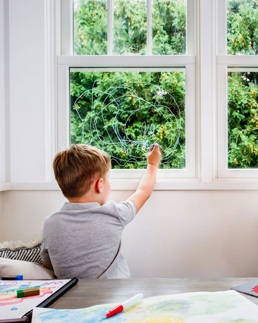 2 children crouched down drawing a town scene on a large piece of paper